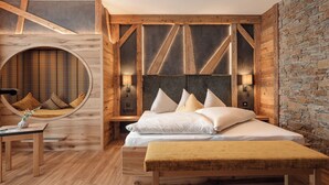 A bedroom with a bed, bedside tables, a round mirror, and a bench. - Aktiv und Welnesshotel Kohlerhof  (Fuegen)