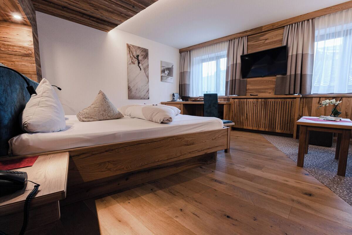Ein modernes Hotelzimmer mit einem hölzernen Bett, einem Schreibtisch, einem Fernseher und einem großen Fenster mit Vorhängen.
