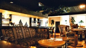 A cozy lounge area with a sofa, a round wooden table, and a bar area in the background. - Edelweiß (Goetzens)