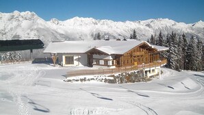 A wooden lodge with a snow-covered roof, set against a backdrop of snow-covered mountains. - Edelweiß (Goetzens)