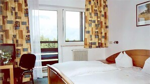 A hotel room with a bed, a desk, a chair, and a window with curtains.