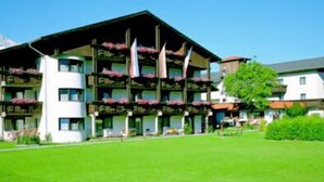 A multi-story hotel with balconies, a green lawn, and a clear blue sky.