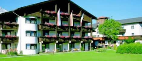 A multi-story hotel with balconies, a green lawn, and a clear blue sky.