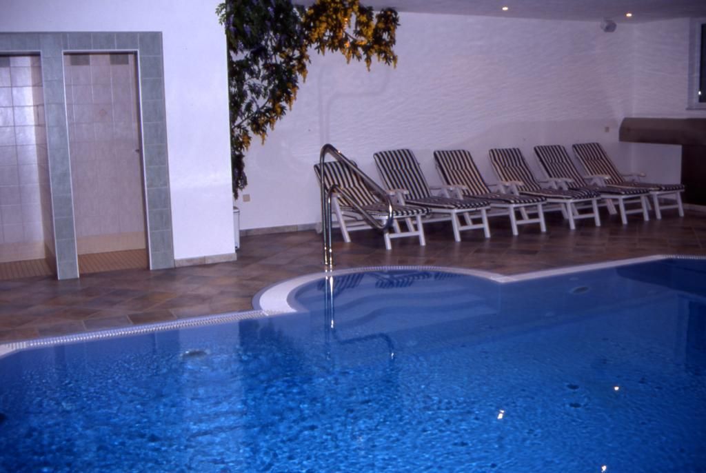 Piscina interna com superfície de água cristalina, rodeada por espreguiçadeiras.