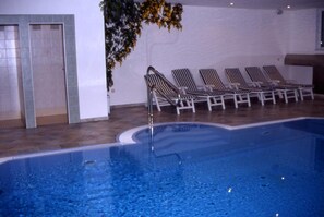 Una piscina interior con superficie de agua cristalina, rodeada de sillones de descanso.