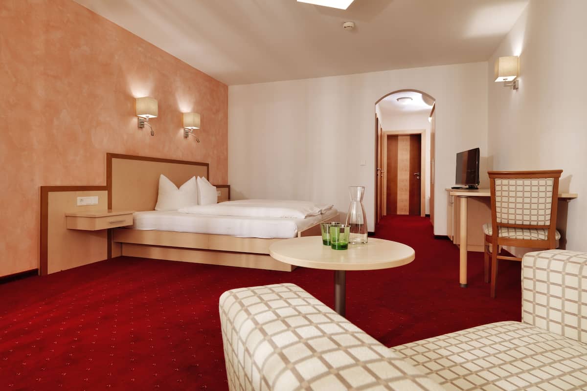 Une chambre d’hôtel avec un lit, une table de chevet, une lampe, une chaise et une petite table avec une boisson.