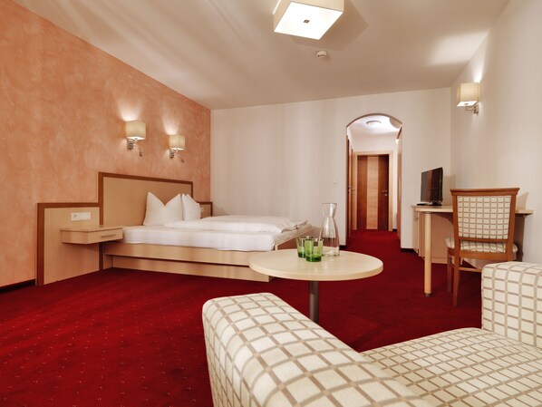 A hotel room with a bed, bedside table, lamp, chair, and a small table with a drink.