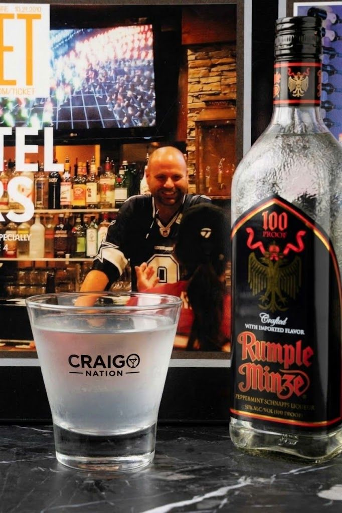 Baarimainen ympäristö, jossa on Craig's Nation -logolla varustettu lasi, pullo Rumple Minze -likööriä ja henkilö, jolla on urheiluseuran pelipaita päällään.