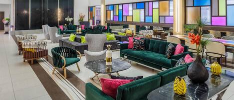Un vestíbulo amplio con varias zonas de estar, un ventanal con paneles de colores y una decoración de diseño moderno.