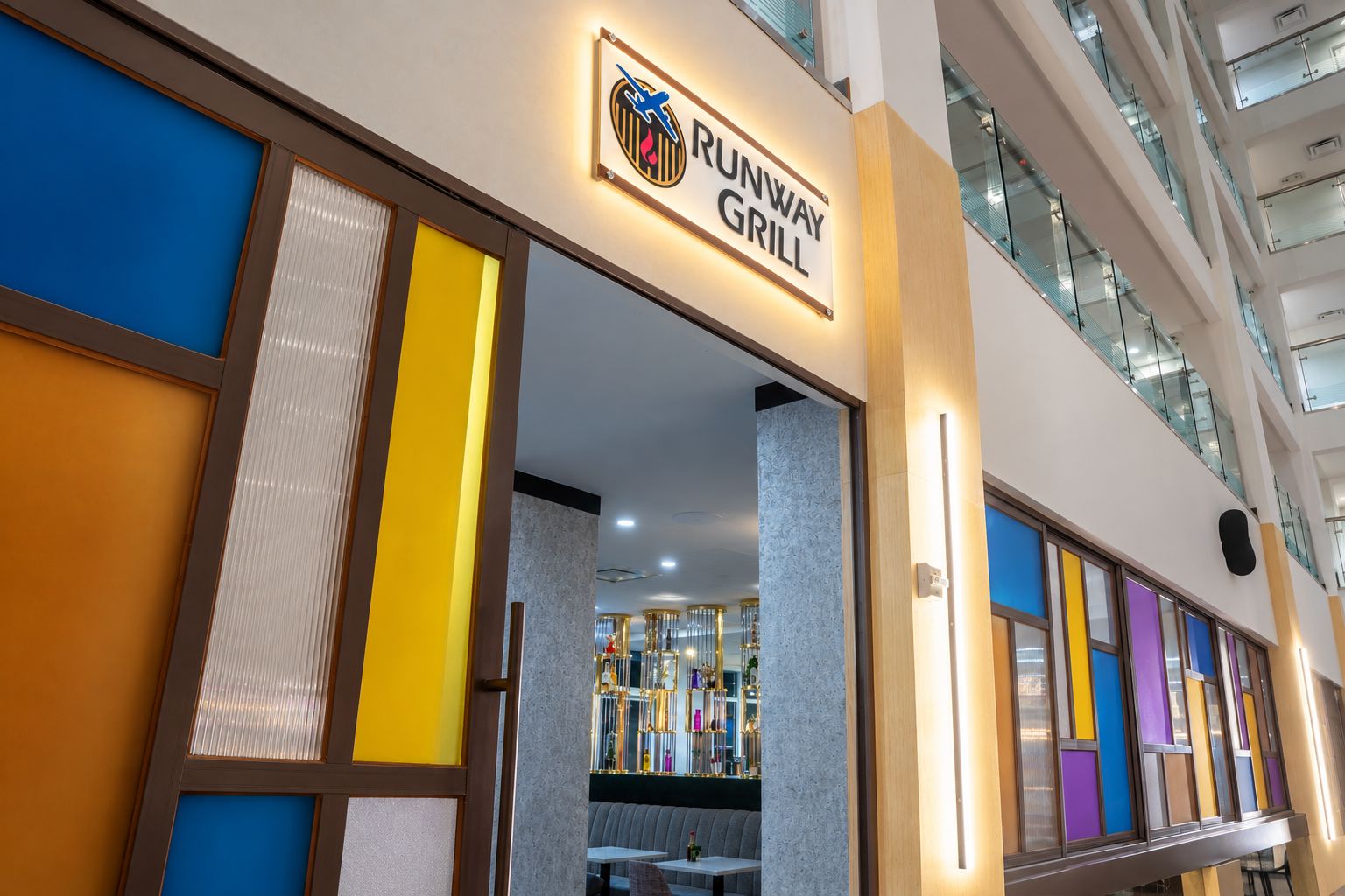 A modern interior with a sign for 'Runway Grill' and a glass railing on the upper level.