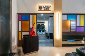 A modern interior with a reception desk, a sign for 'Runway Grill,' and a seating area with a green sofa and a small table.