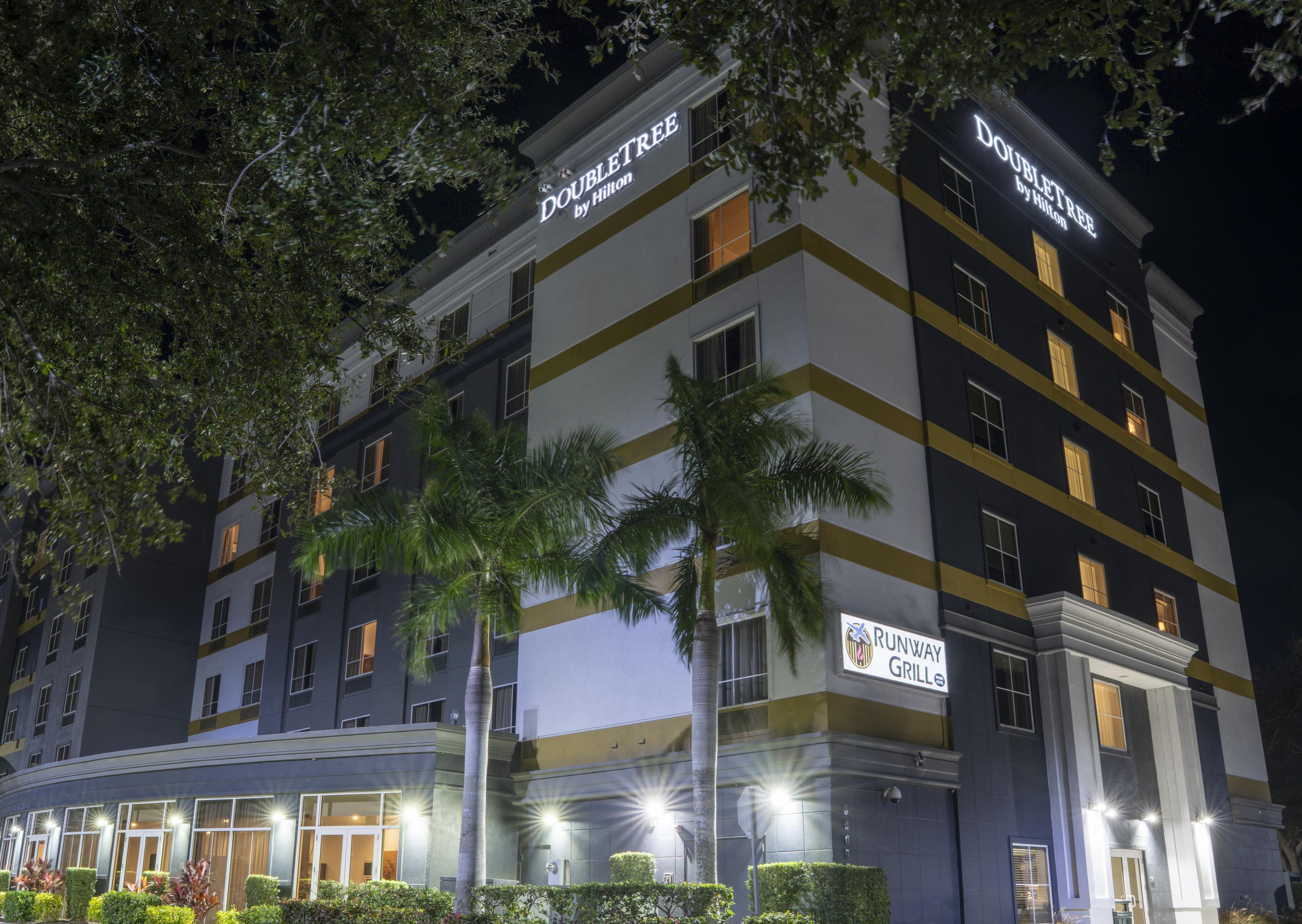A multi-story hotel with 'DOUBLETREE by Hilton' signage, a 'RUNWAY GRILLE' sign, and a palm tree in the foreground.
