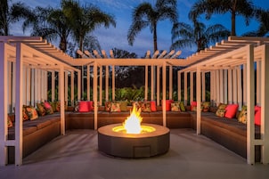 A circular fire pit surrounded by a covered seating area with a view of palm trees.