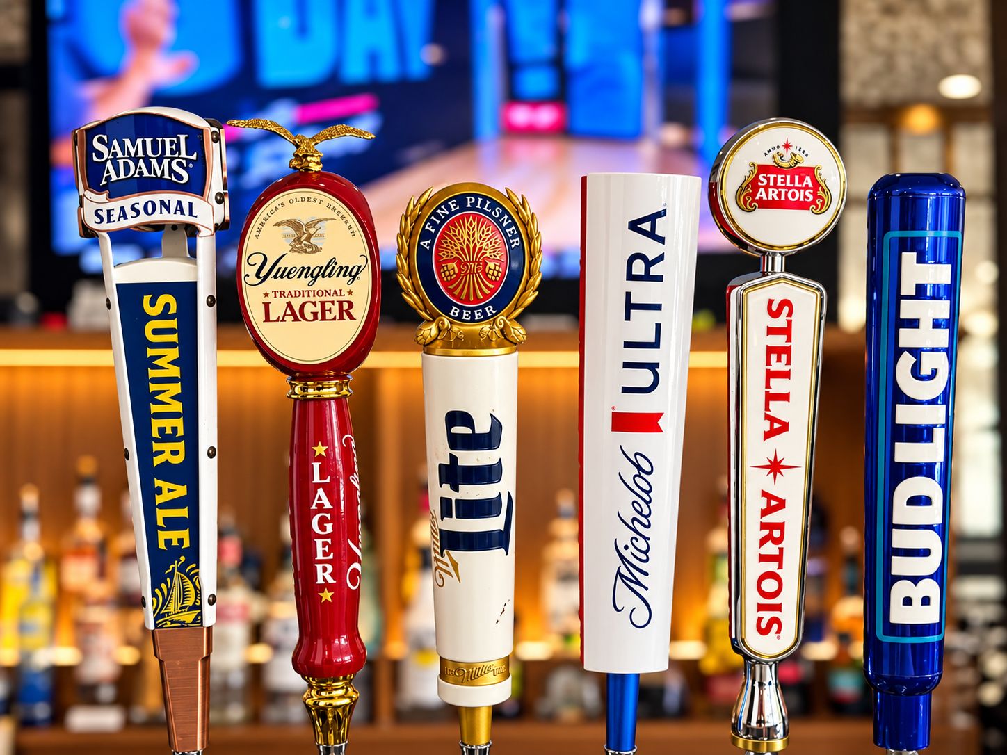Une rangée de robinets à bière avec des étiquettes indiquant les marques suivantes : Samuel Adams, Yuengling, Miller Lite, Michelob, Stella Artois et Bud Light.
