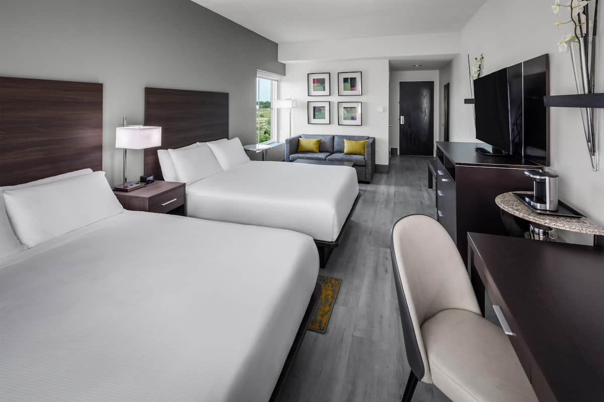Een hotelkamer met twee bedden, een bureau met een flatscreen televisie, een bank en een lamp.