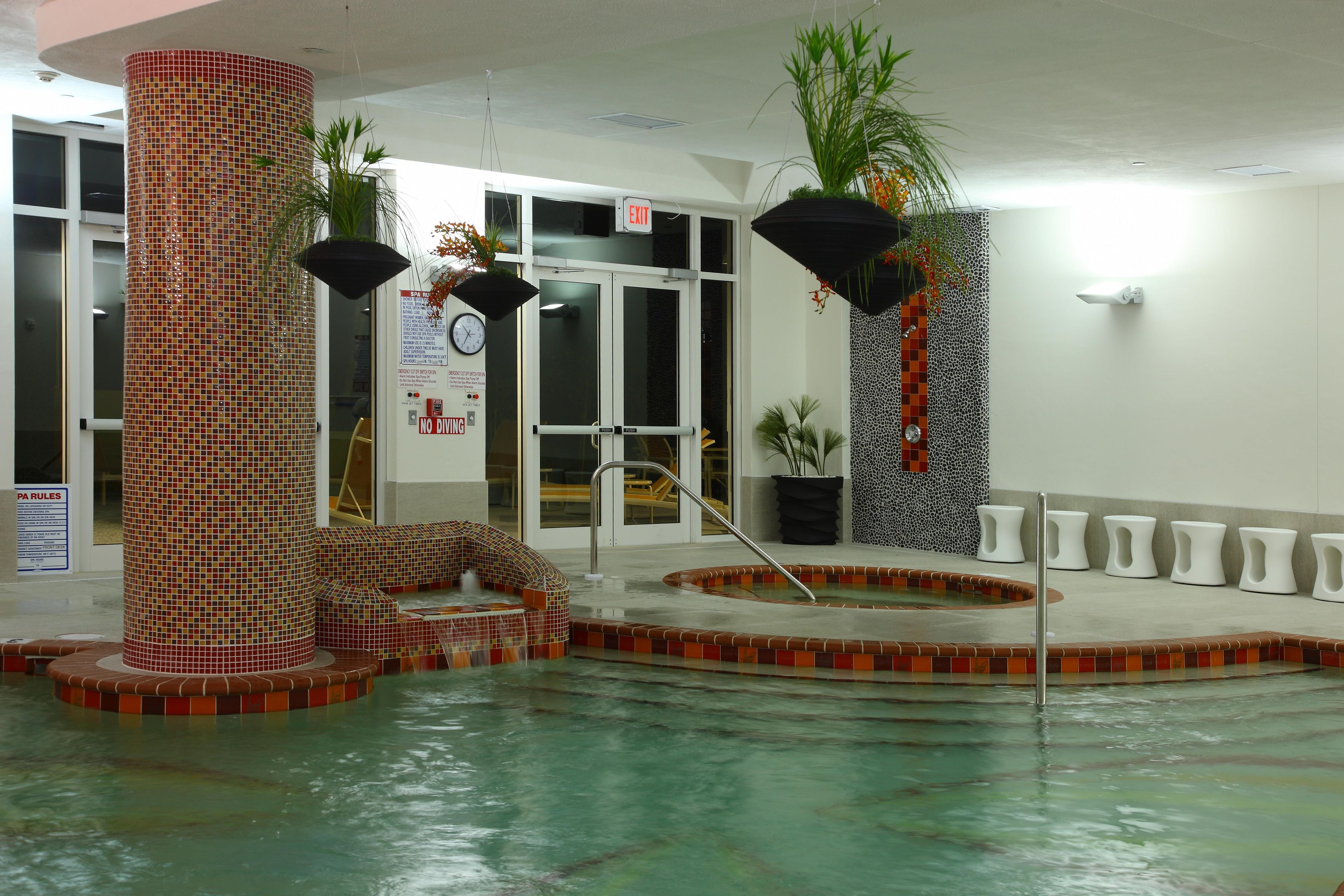 An indoor swimming pool with a tiled wall, a hot tub, and a seating area.