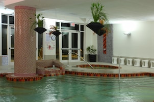 Una piscina interior con pared de azulejos, un jacuzzi y una zona de estar.