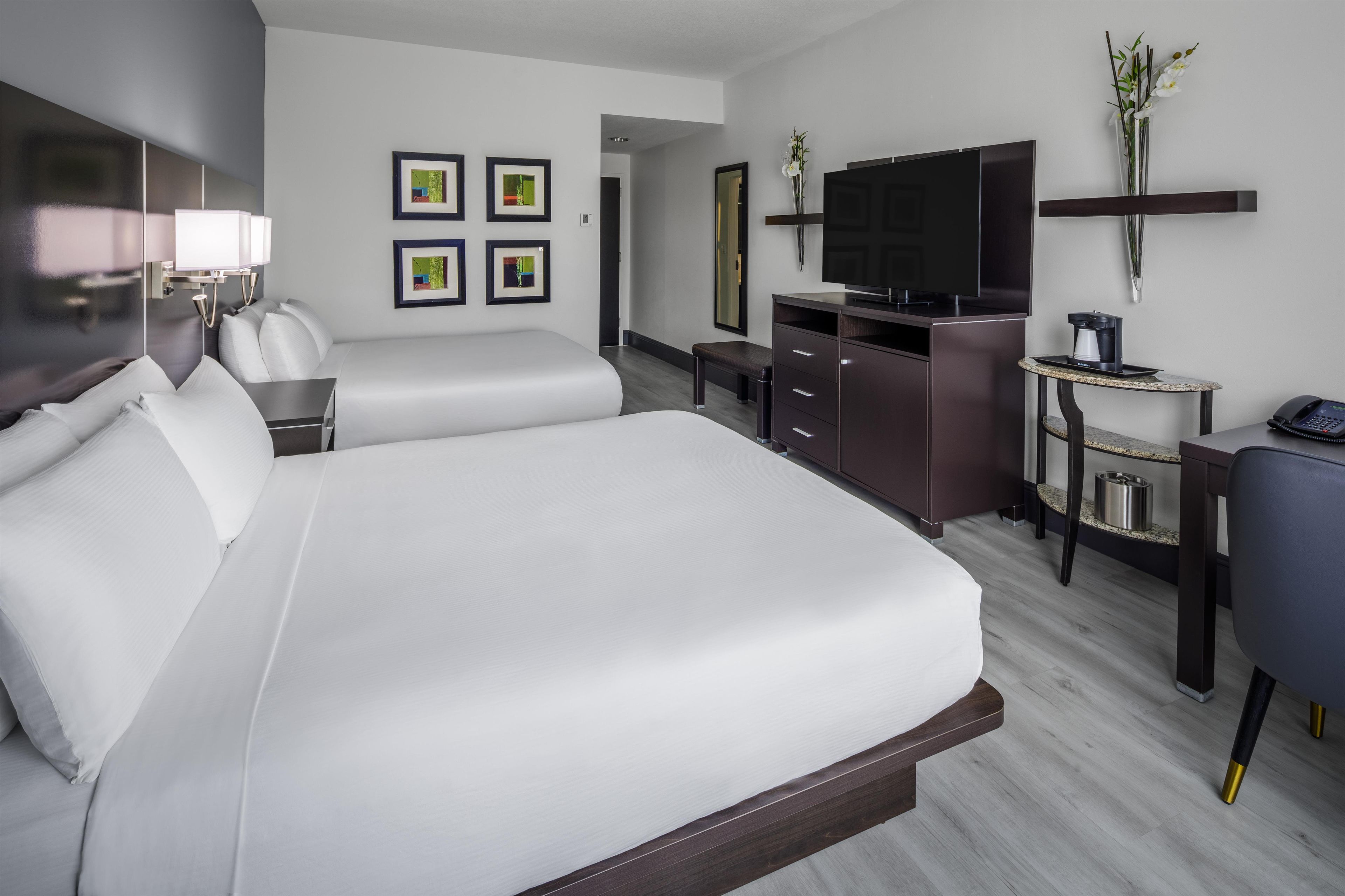Habitación de hotel con una cama grande, un escritorio, una silla, un televisor y obras de arte en la pared.