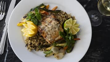 A plate with grilled fish, rice, and vegetables on a dark marble table.