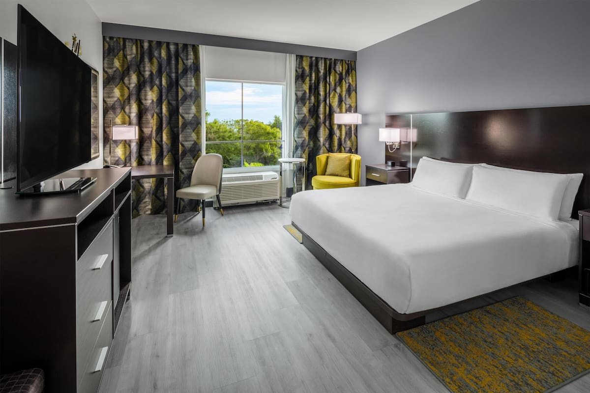 Een hotelkamer met een groot bed, een bureau met een televisie, een stoel en een raam met gordijnen.