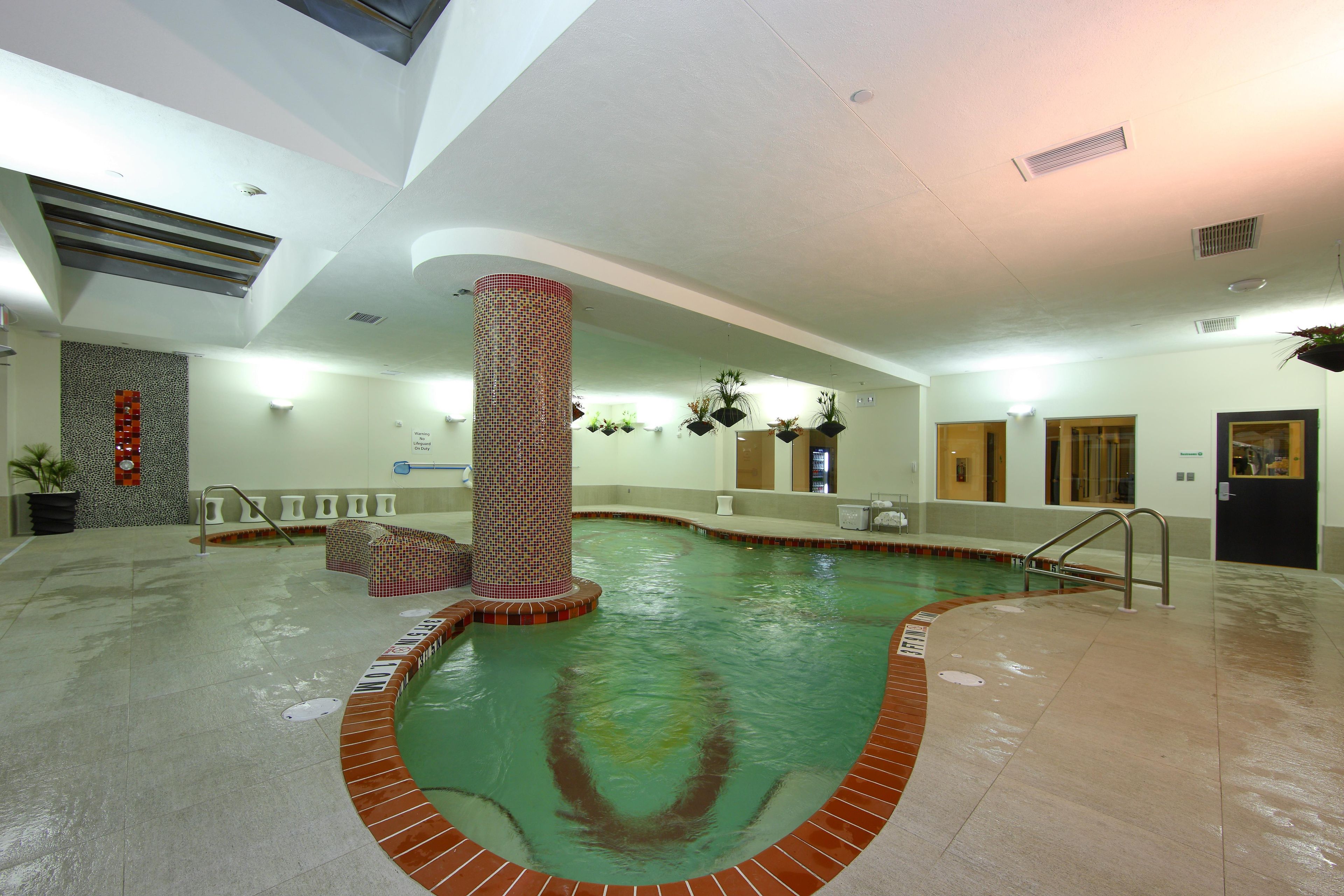 Una piscina interior con pared de azulejos, una columna central y suelo de baldosas.