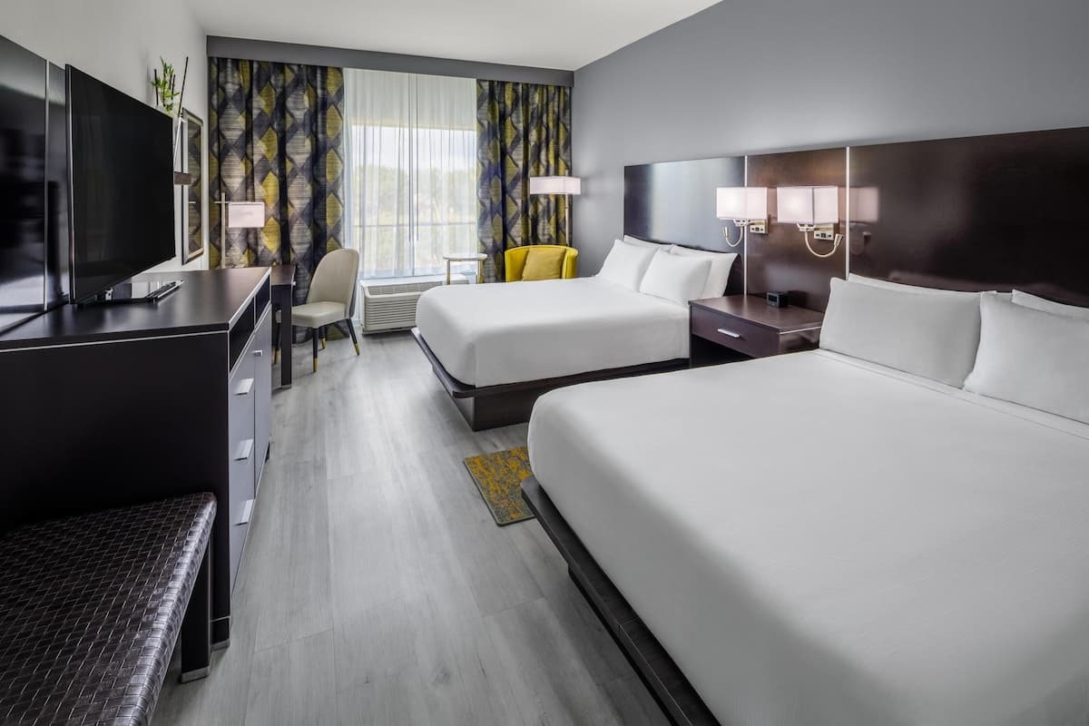 Een hotelkamer met een televisie, twee bedden, een bureau, een stoel en een raam met gordijnen.
