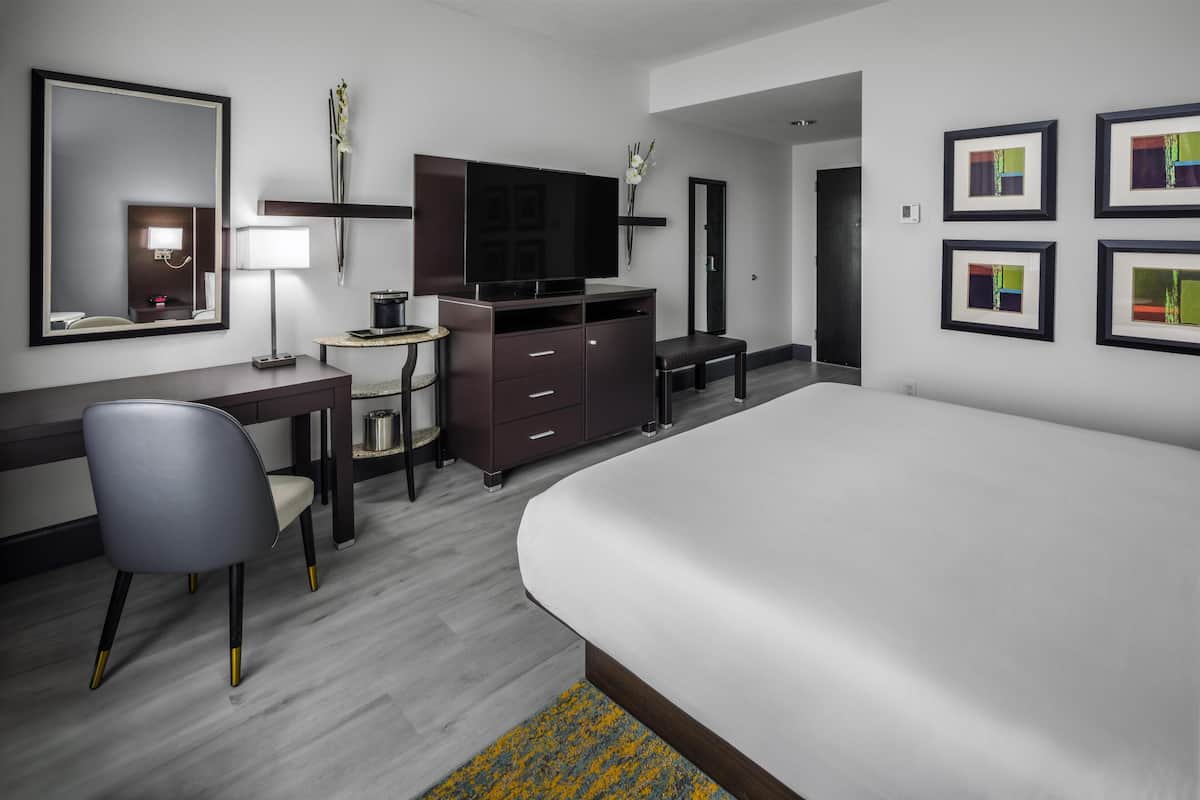 Een hotelkamer met een bed, bureau, stoel, televisie en kunst aan de wanden.