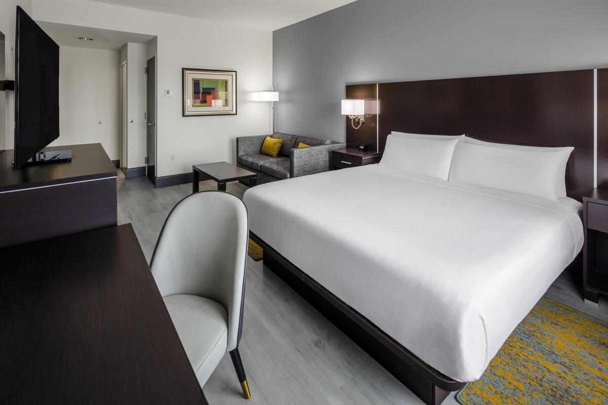 Een hotelkamer met een groot bed, een bureau, een stoel, een bank, een televisie en een lamp.