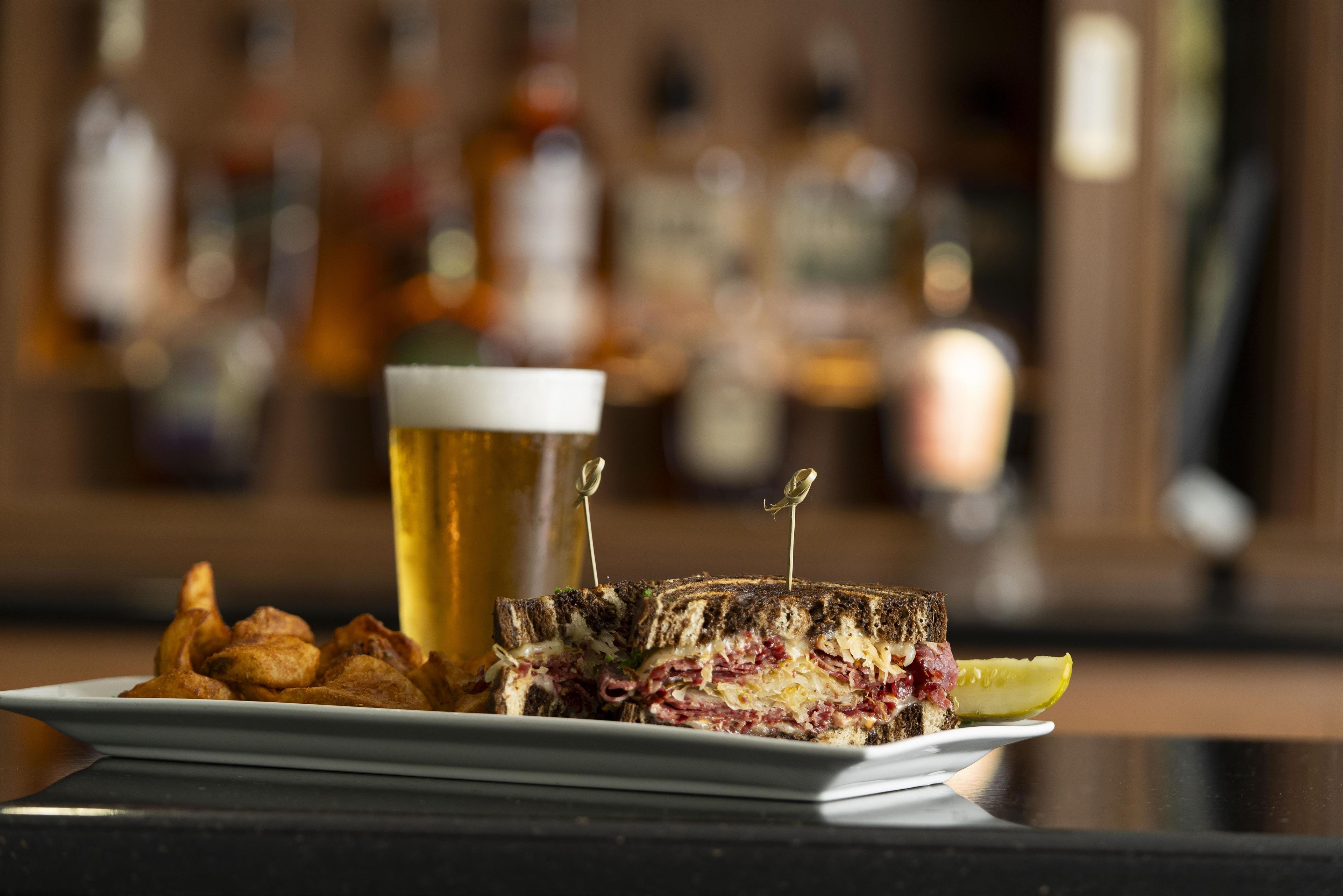 Ein Sandwich mit Zahnstochern, ein Bierglas und Chips auf einem Teller.