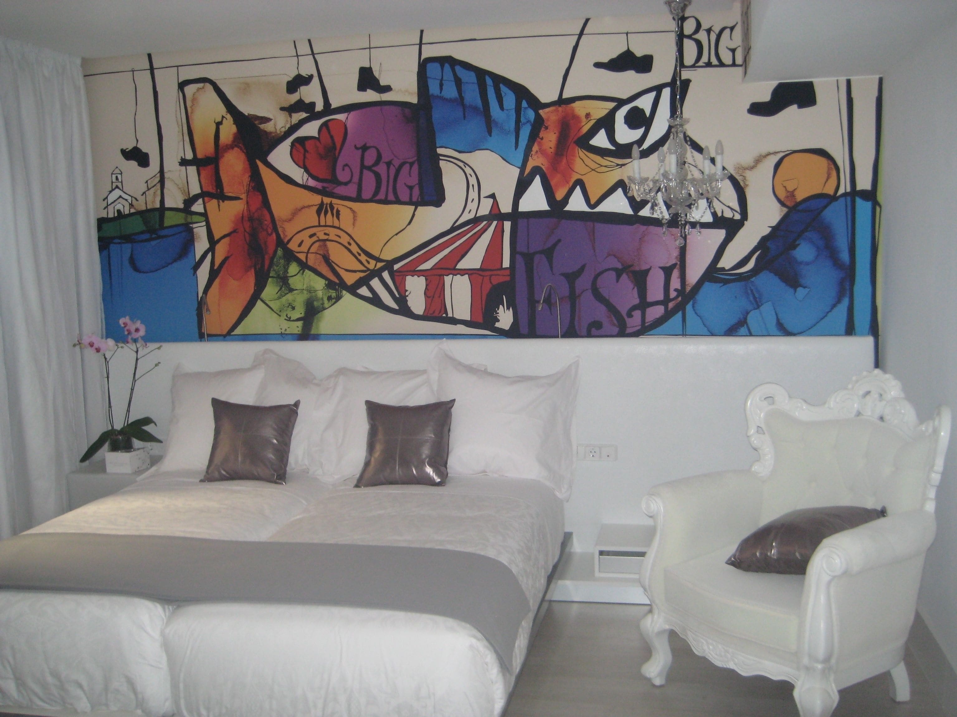 Un dormitorio con una cama grande, un sillón blanco y un cuadro abstracto colorido en la pared.