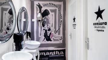 A modern bathroom with two sinks, a large mirror, and a poster on the wall.