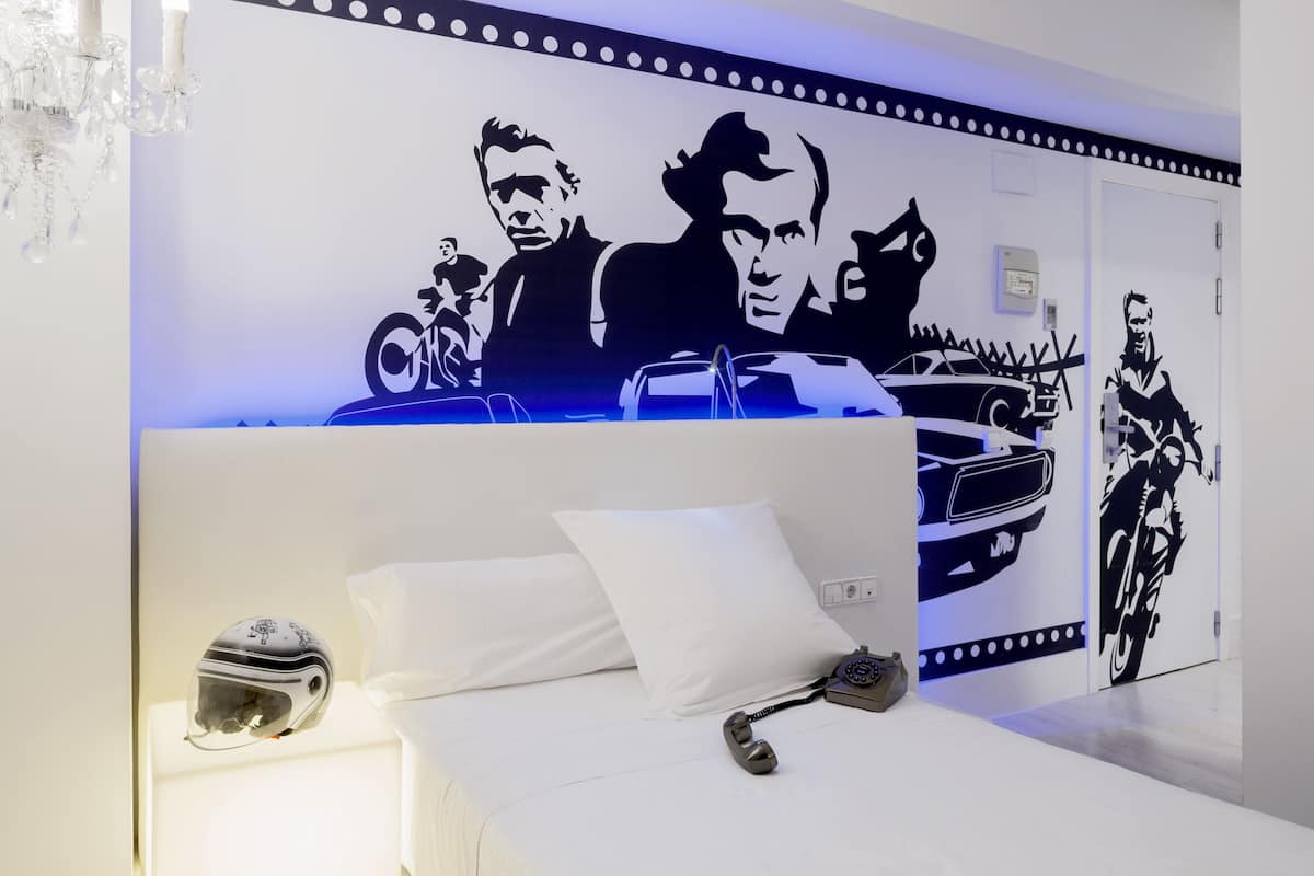 Ein modernes Schlafzimmer mit einem großen Bett, einem Nachttisch, einem Motorradhelm und einem Vintage-Telefon.