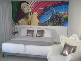 Un dormitorio con una cama grande, dos almohadas, un sofá blanco y un mural colorido en la pared.