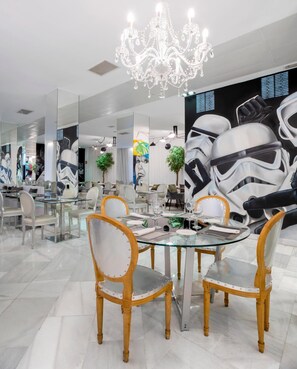 A modern dining area with glass tables and wooden chairs, a chandelier, and Star Wars-themed wall art.