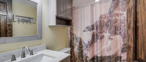 Ein Badezimmer mit einem großen Waschbecken, einer Toilette und einer Duschkabine mit einer Berglandschaft.