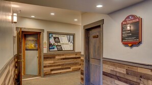 A hotel reception area with a wooden reception desk, a signboard with room information, and a staircase leading to the main floor. - Der Steiermark (Breckenridge)