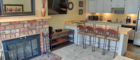 Una cocina con chimenea, televisor y zona de bar con taburetes.