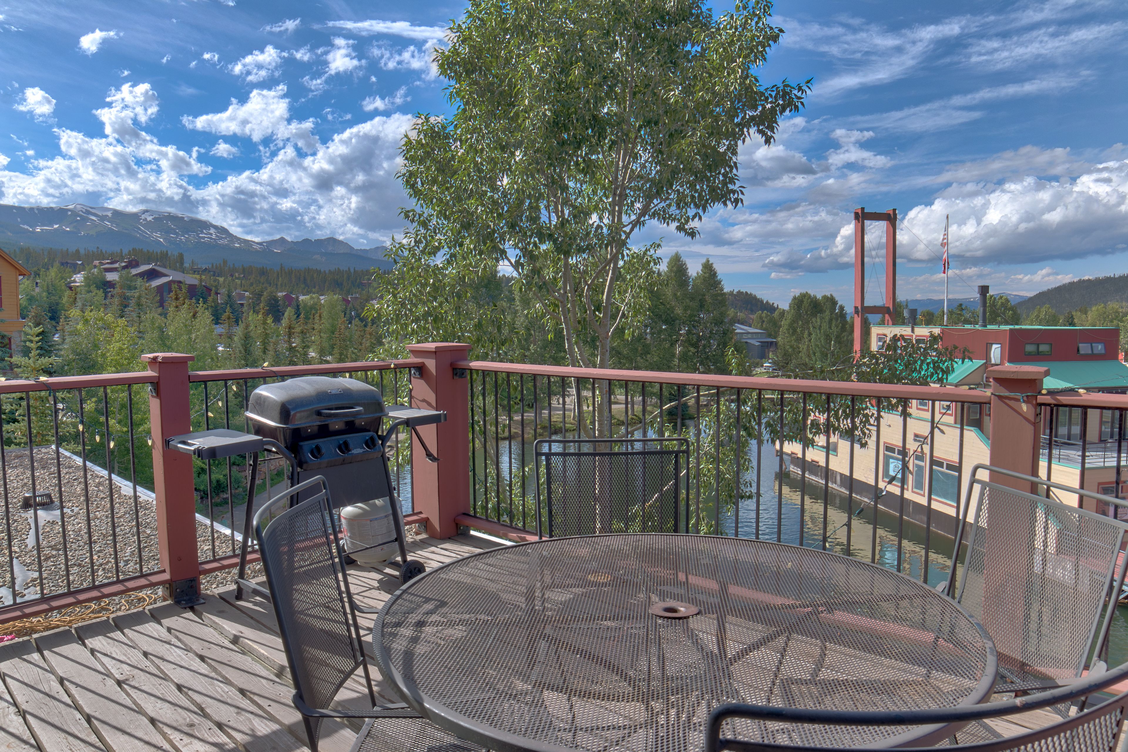A balcony with a grill, chairs, and a view of a lake and mountains.