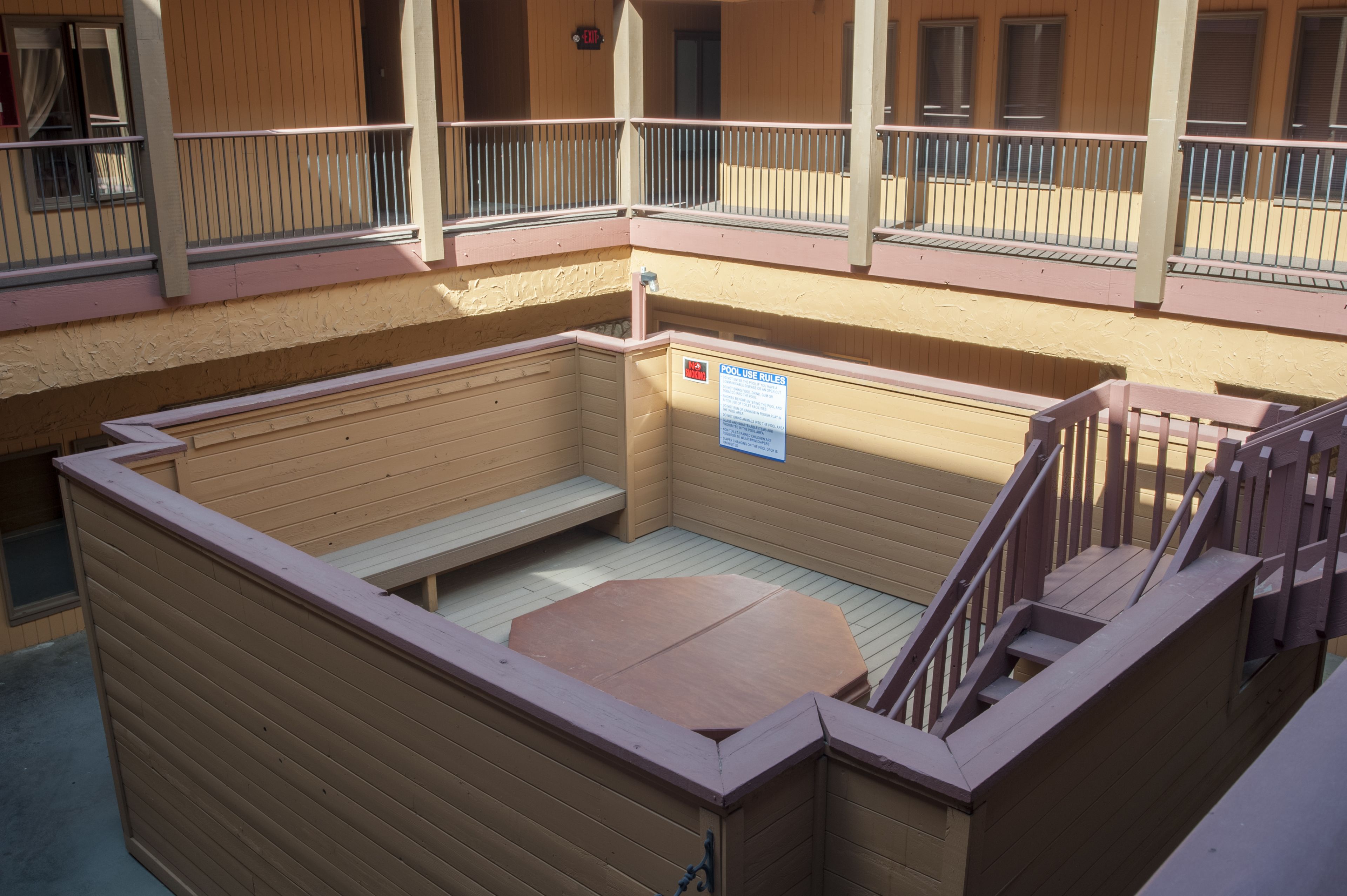 Zona de piscina con terraza de madera, un banco y un cartel con las normas de uso de la piscina.