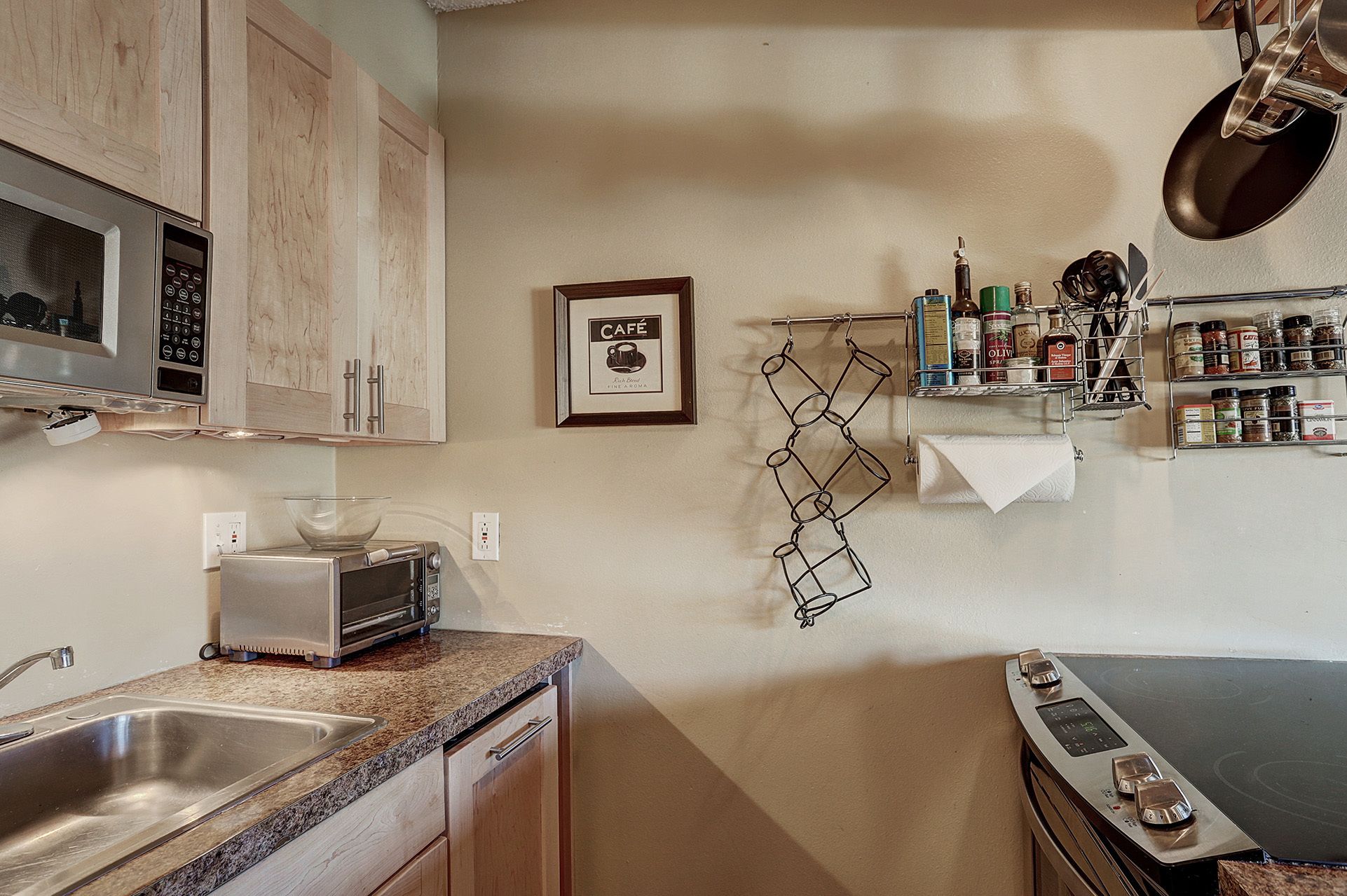 A kitchen with a microwave, toaster, sink, and stove. There is a framed picture of a coffee cup on the wall.