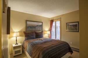 Un dormitorio con una cama, dos lámparas de noche, un cuadro en la pared y una ventana con cortinas.