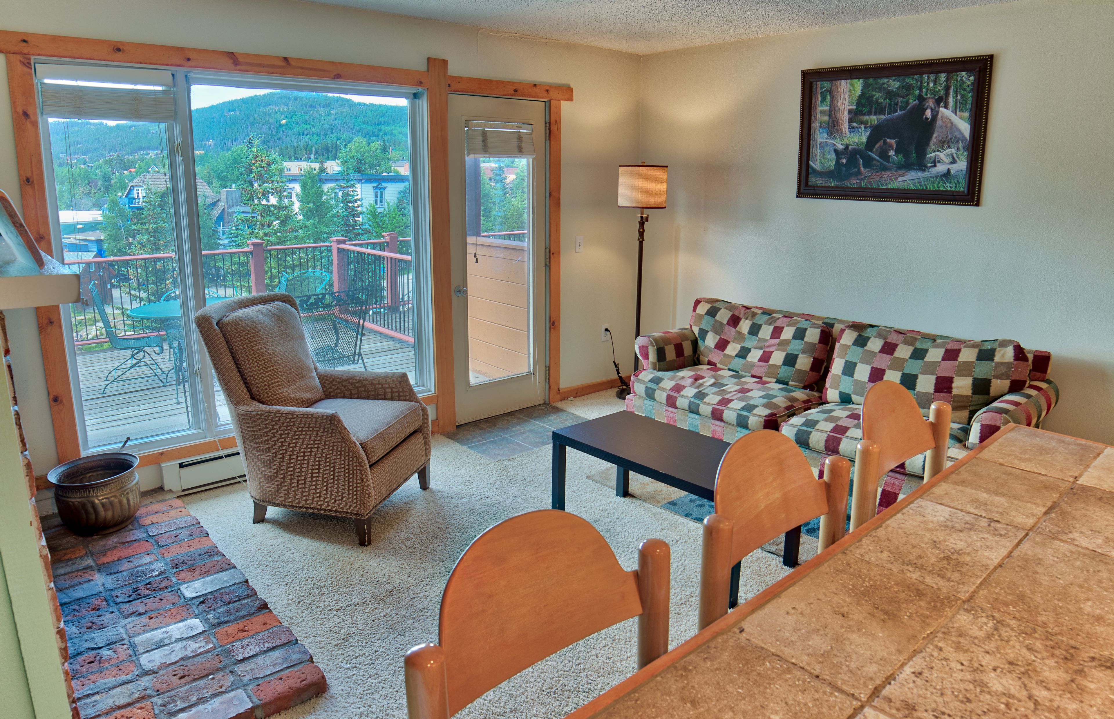 A cozy living room with a large window, a sofa, a chair, a table, and a view of a balcony.
