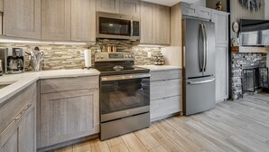 A modern kitchen with wood-paneled cabinets, a stainless steel refrigerator, a built-in oven, and a stone fireplace. - Der Steiermark (Breckenridge)