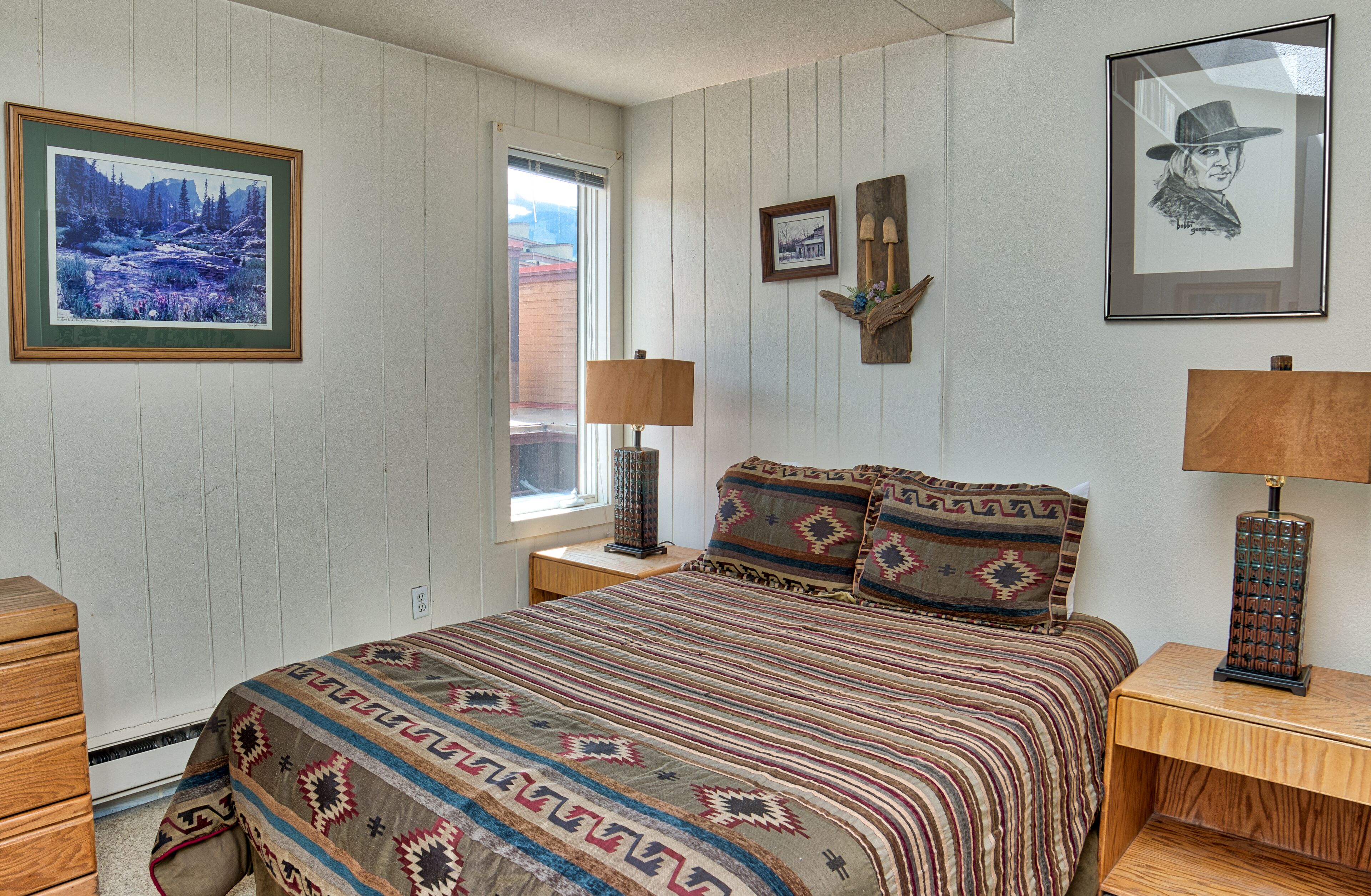 A bedroom with a bed, two nightstands, a dresser, and a window with a view.