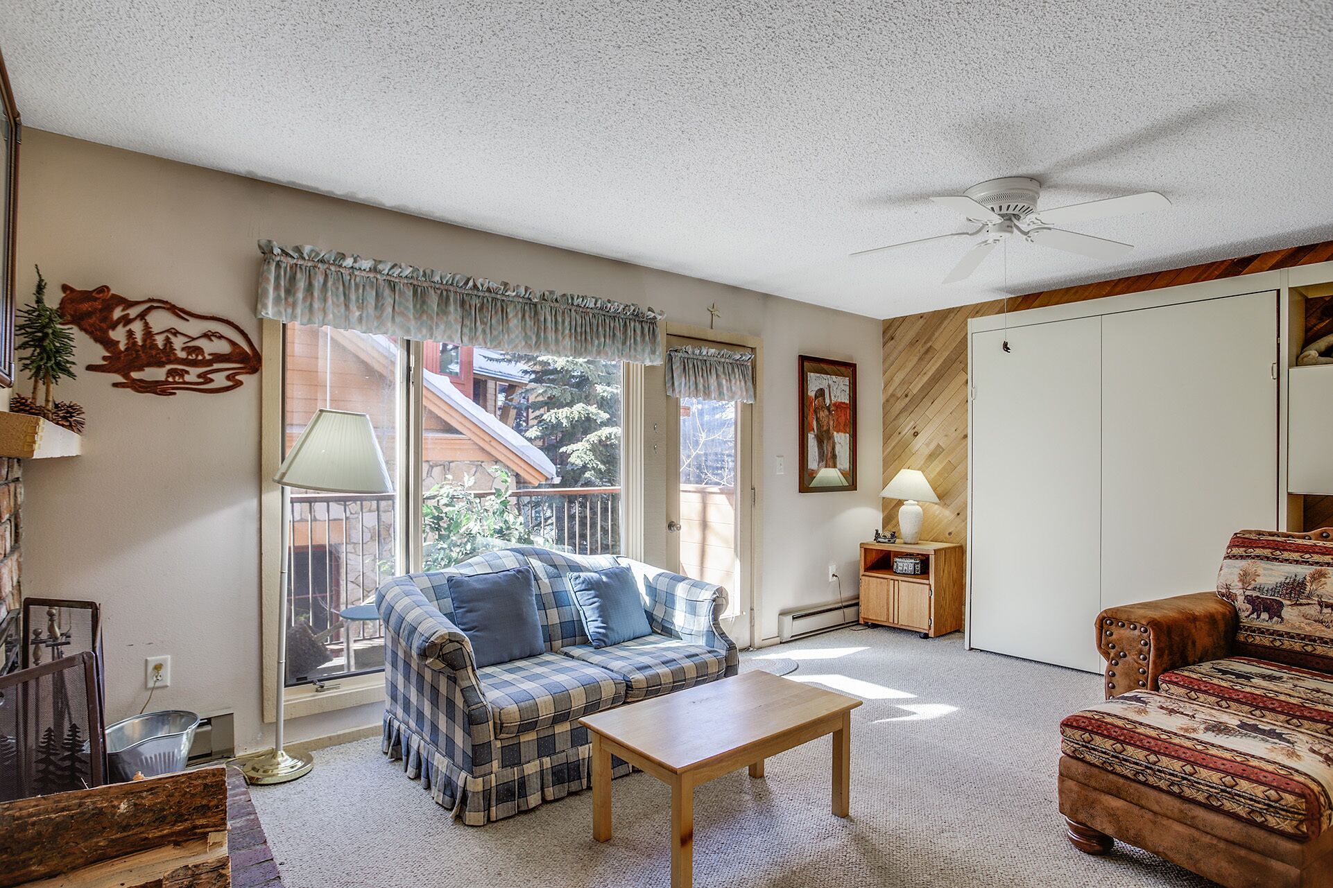 Ein gemütliches Wohnzimmer mit einem Karomuster-Sofa, einem Holztisch und einem Deckenventilator.