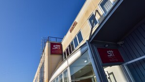A hotel with a clear sky, featuring a red sign with the hotel's name and logo. - Standard Hotel Udine (Pradamano)