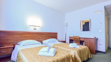 Camera d'albergo con due letti, una scrivania, una sedia e uno specchio.