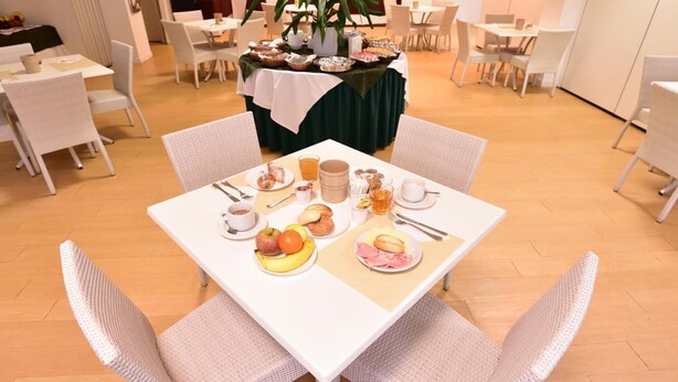 A dining area with a table set for breakfast, including fruits, pastries, and beverages. - Standard Hotel Udine (Pradamano)