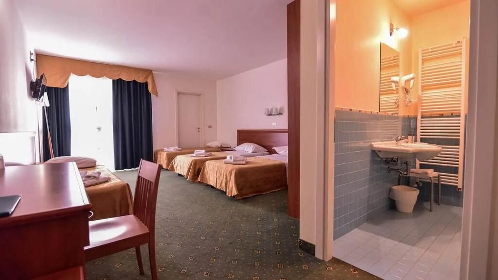 Ein Hotelzimmer mit Esstisch, zwei Betten und einem Badezimmer inklusive Waschbecken und Handtuchhalter.