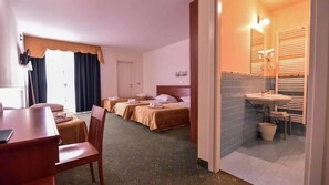 A hotel room with a dining table, two beds, a bathroom with a sink and towel rack.